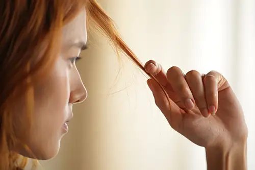Женщина смотрит на свои волосы